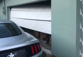 White garage door dislodged and hanging unevenly off the track in Buda garage