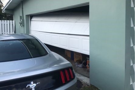 White garage door dislodged and hanging unevenly off the track in Buda garage