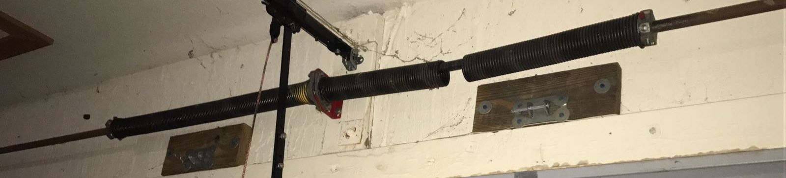 Close-up of a broken garage door extension spring above a gray sectional door in a Jonestown home garage.